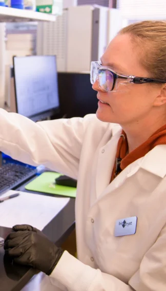 A person wearing safety goggles and a lab coat works in a laboratory, using scientific equipment.